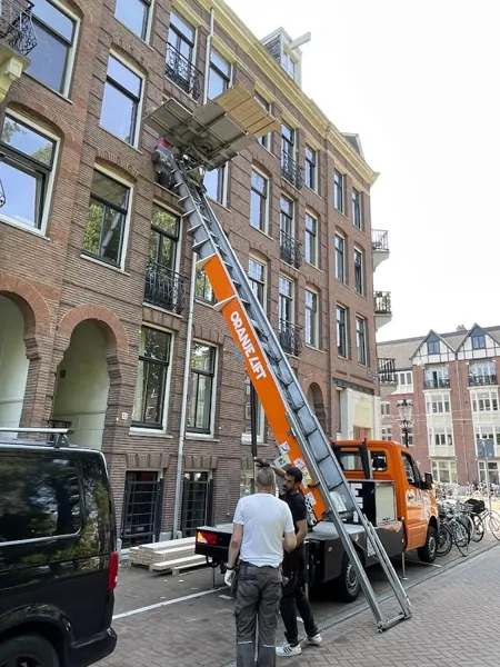 Ladderlift op OranjeLift-vrachtwagen naar bovenste etage van bakstenen pand. Een appje, en je verhuislift in de regio is geregeld.