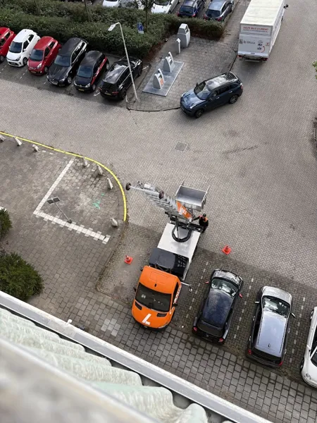 Van bovenaf gezien: OranjeLift-vrachtwagen met ladderlift omhoog op een parkeerplaats. Een appje, en je verhuislift in de regio is geregeld.