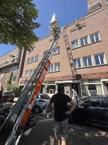 Rode bakstenen flat met aanhangerlift naar de bovenste etage, verhuizer bij bediening. Bij OranjeLift huur je een verhuislift altijd met operator.