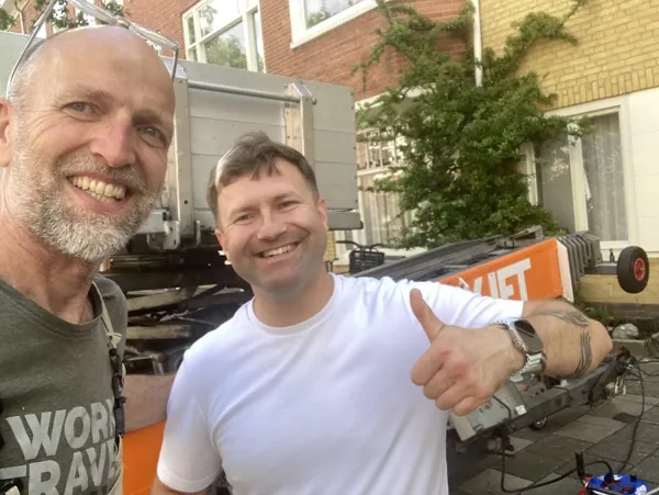Twee lachende mannen op een selfie bij de OranjeLift-aanhangerlift voor een huis. Piano of Amerikaanse koelkast, wij tillen het veilig omhoog.
