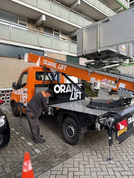 Verhuizer bij de zijkast van de OranjeLift-vrachtwagen voor een flat met balkons. Onze ladderlift hijst zware kasten zo de hoogte in.