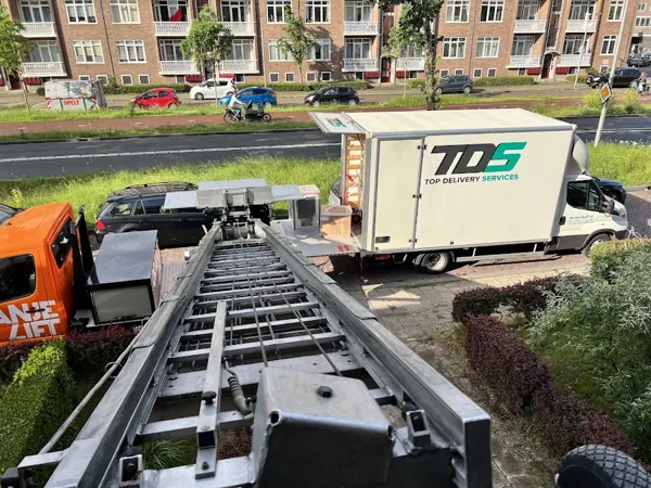 Blik omlaag langs de ladder van de OranjeLift-vrachtwagen naar een bakwagen met dozen. Familiebedrijf dat eerlijk zaken doet tegen een vaste prijs.