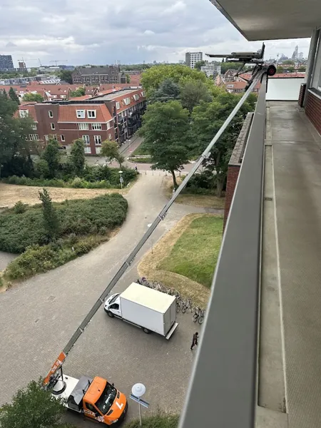 Vanaf een hoge galerij gezien reikt de ladder van de OranjeLift-vrachtwagen tot boven. Onze ladderlift hijst zware kasten zo de hoogte in.