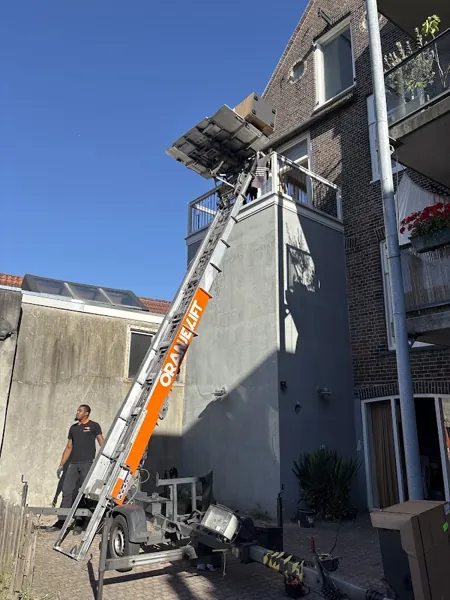 In een achtertuin staat de OranjeLift-aanhangerlift met de ladder naar een dakterras. Een appje, en je verhuislift in de regio is geregeld.