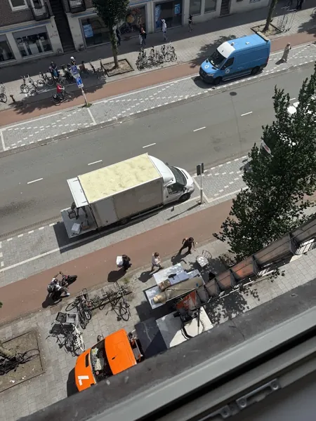 Vanuit een raam: OranjeLift-vrachtwagen en verhuizers op een drukke winkelstraat. Familiebedrijf dat eerlijk zaken doet tegen een vaste prijs.